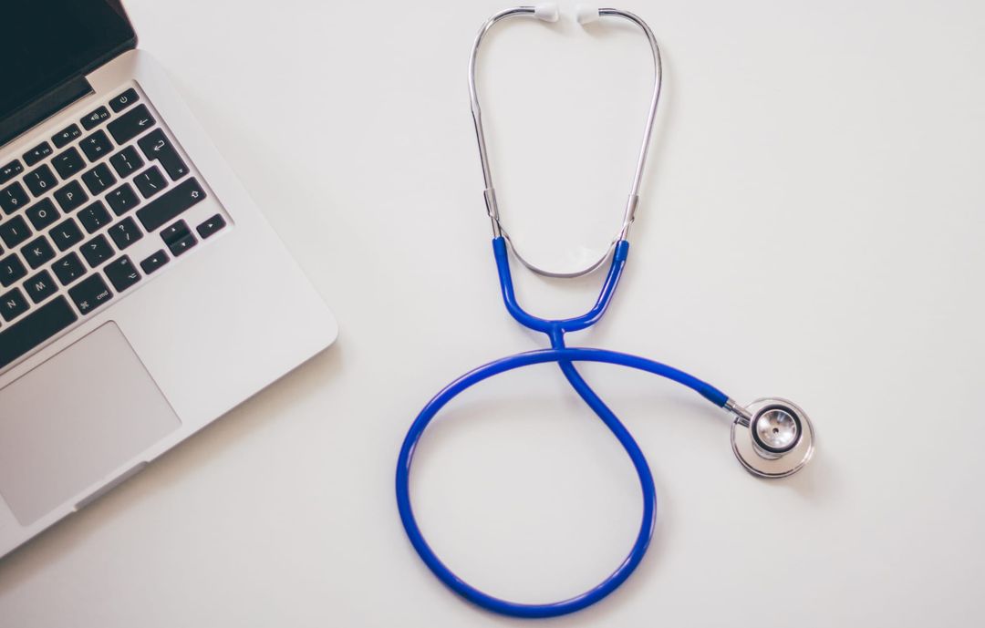 A blue stethoscope beside a laptop on a white desk